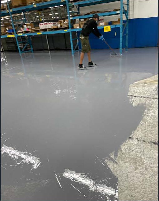 Worker spreading a gray coating across a concrete floor